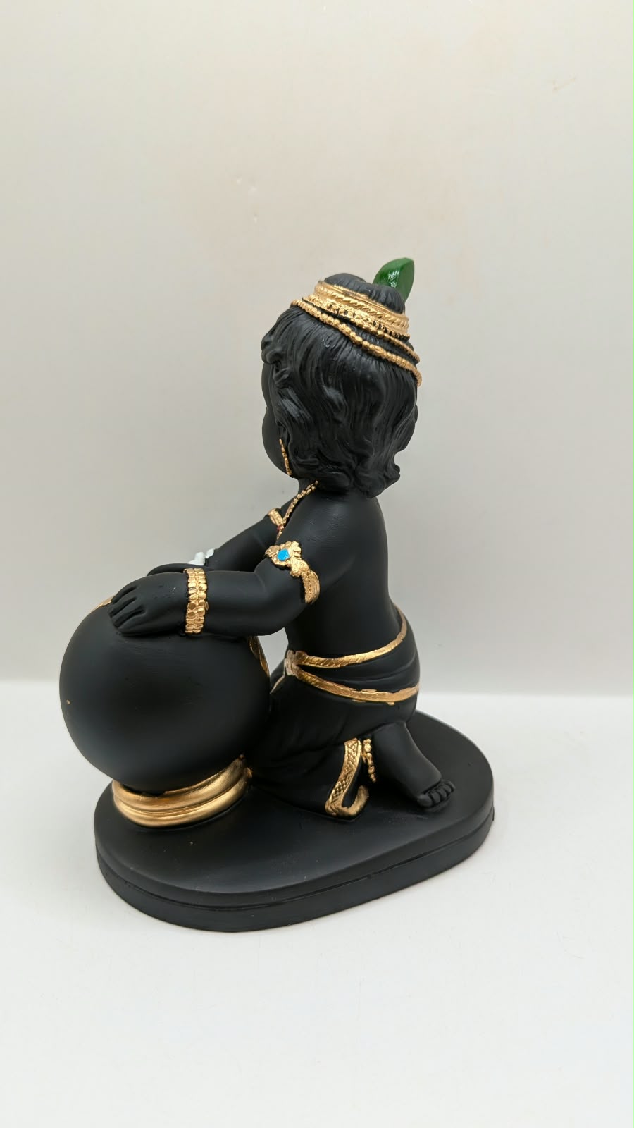 Black and gold baby Krishna statue with butter pot, back view