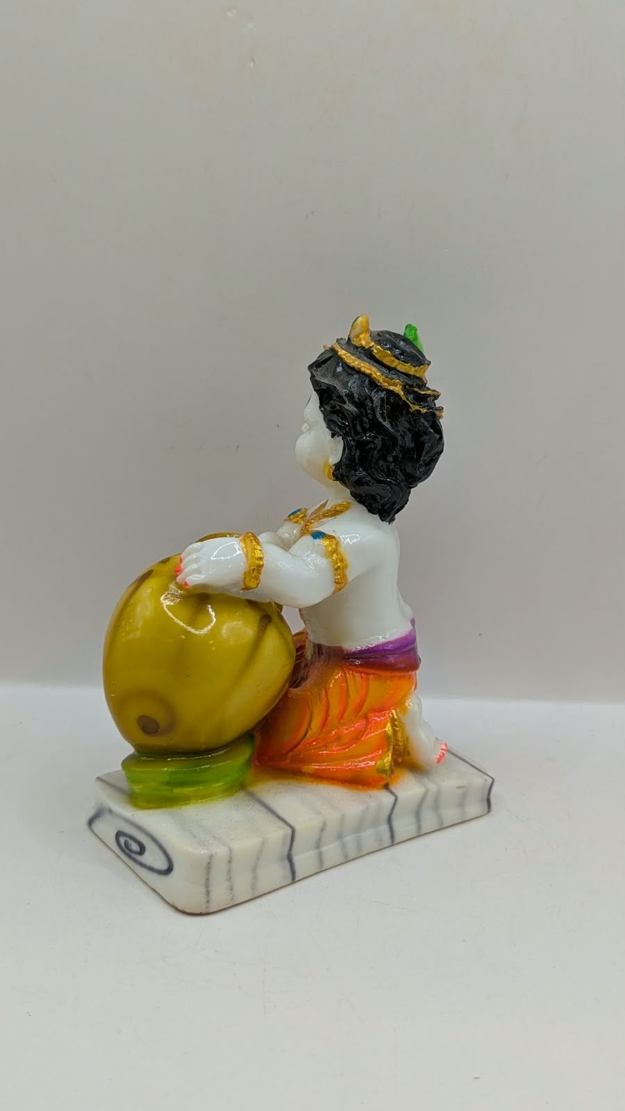 White baby Krishna statue hugging gold butter pot, back view