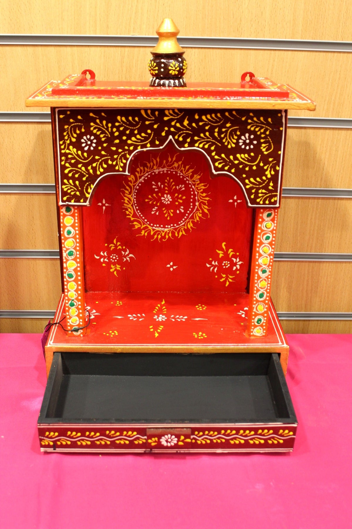 Small red mandir with base drawer open for puja essentials
