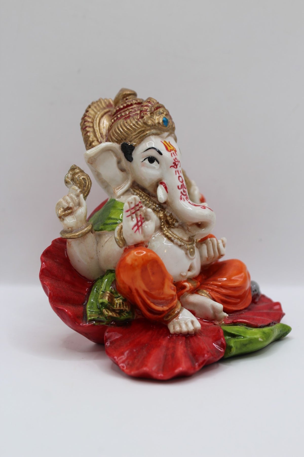 Resin Ganesh murti on red leaf, orange dhoti, left side view