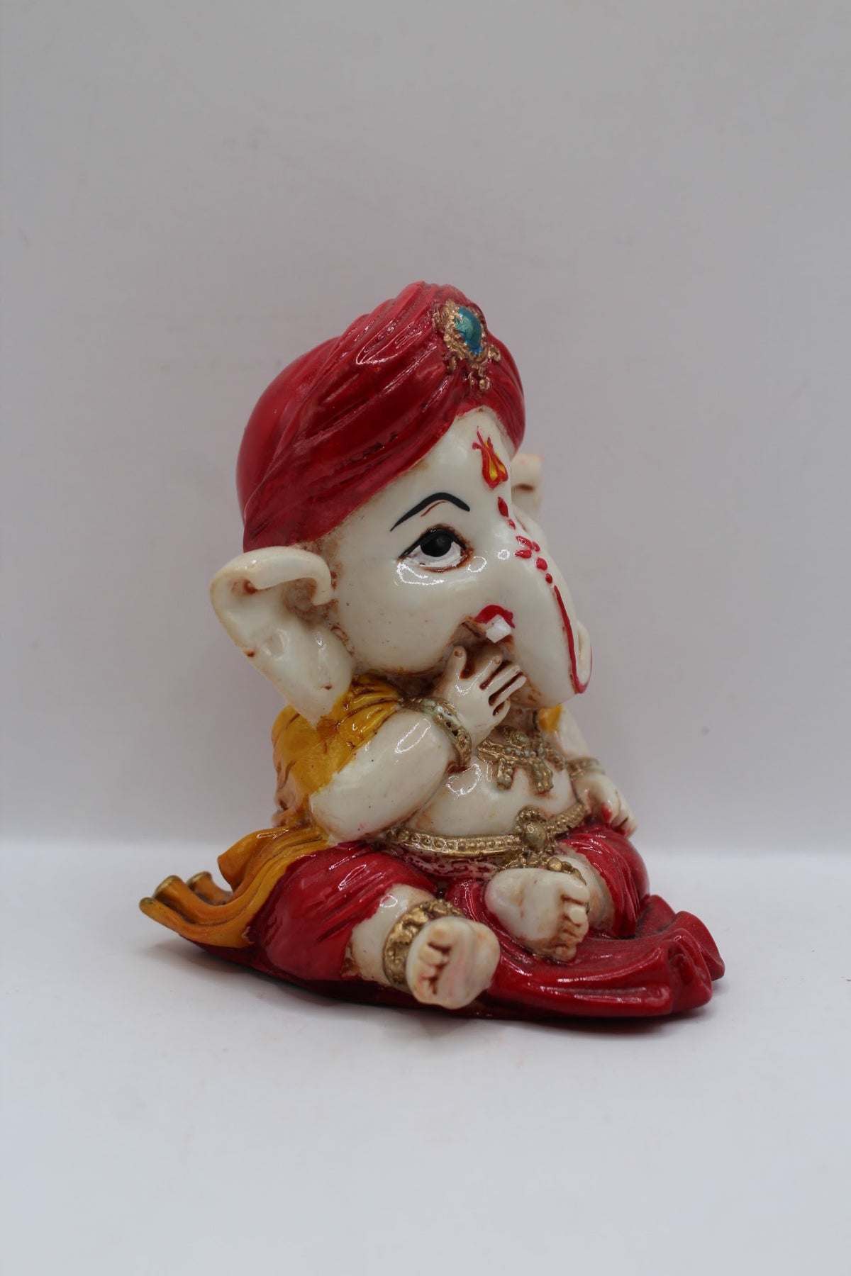 Baby Ganesh murti in red turban, finger to lips, left side view