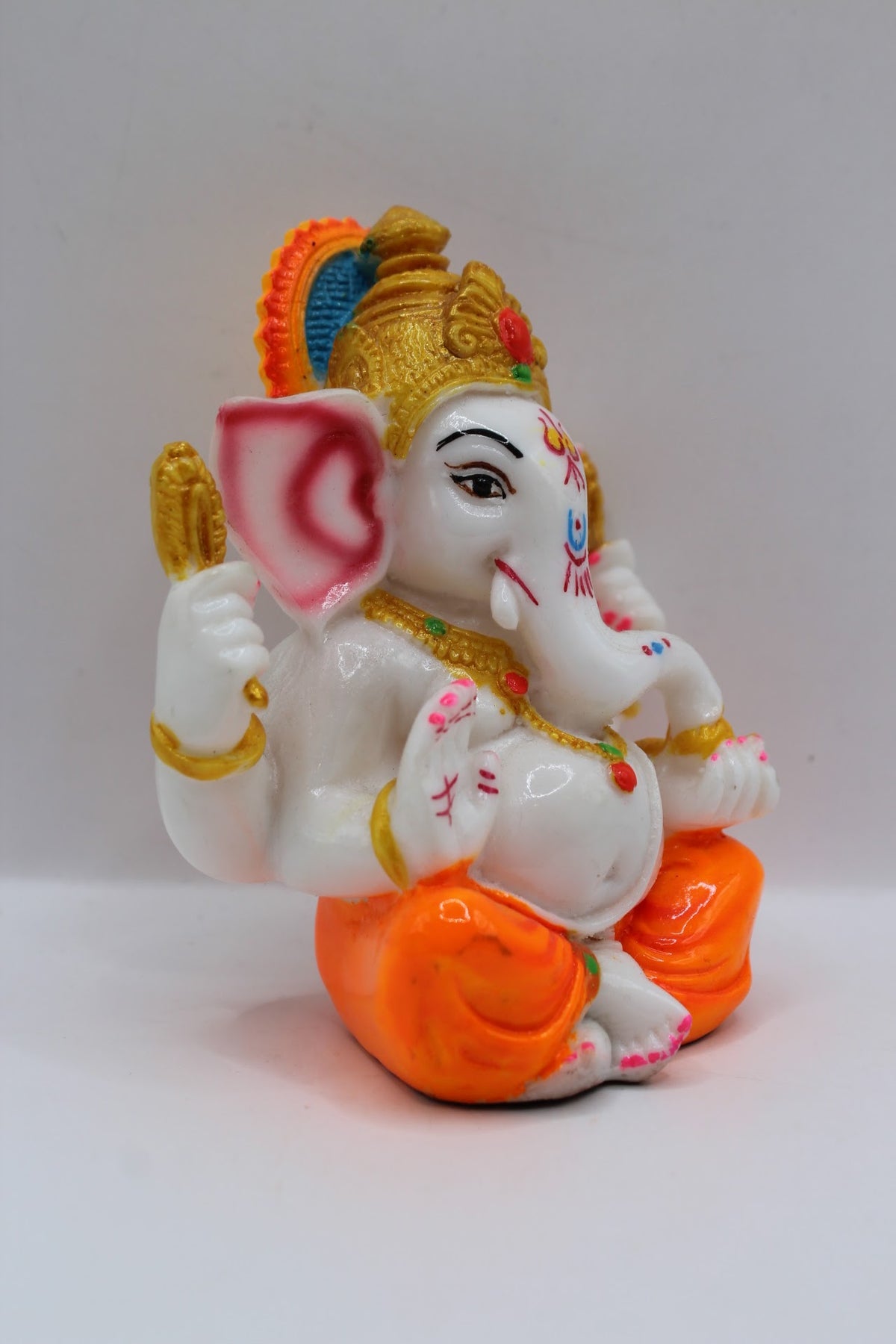 Small white resin Ganesh murti, orange dhoti, left side view