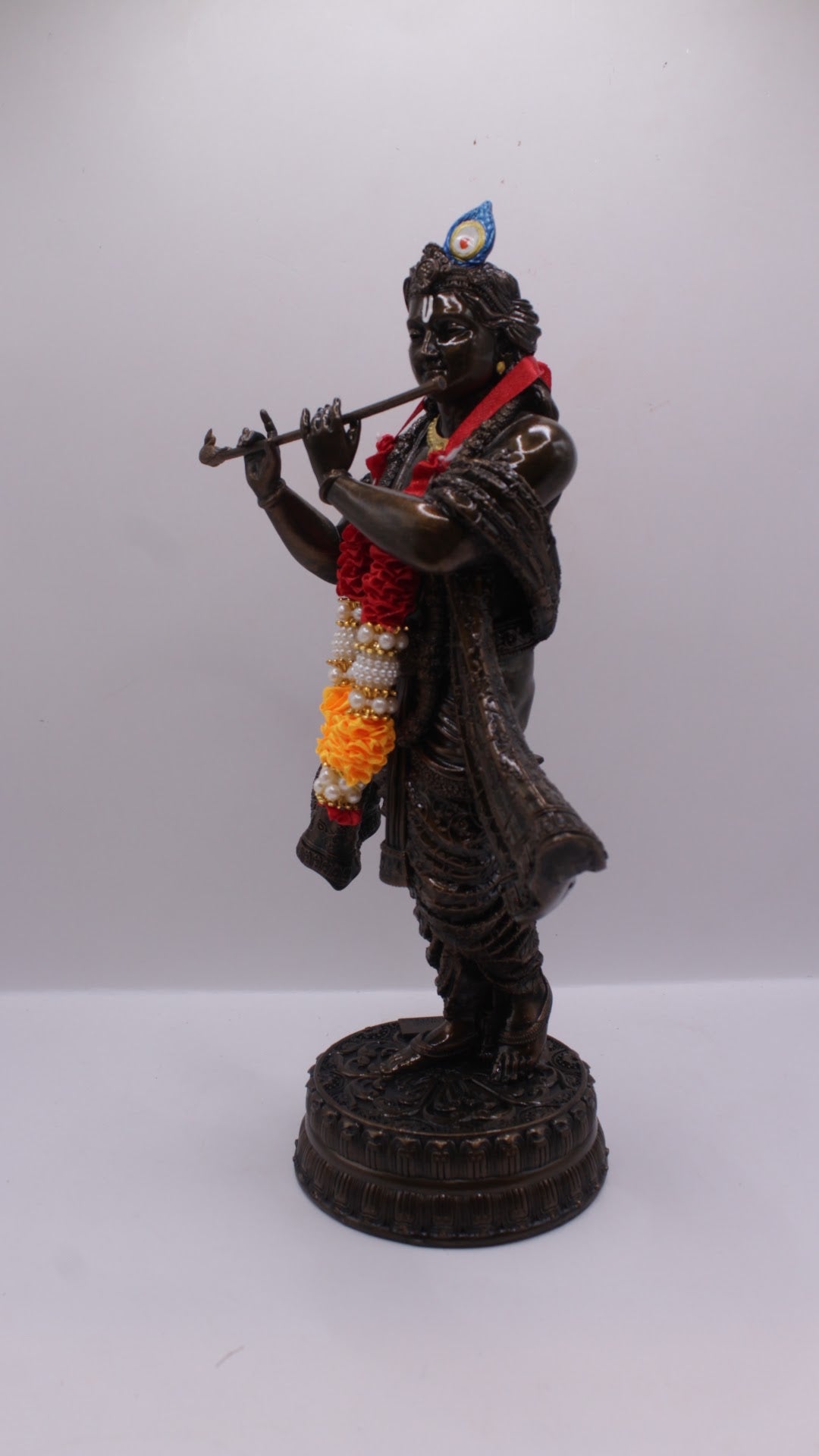 Dark finish resin Krishna statue playing flute, with garland, right side view