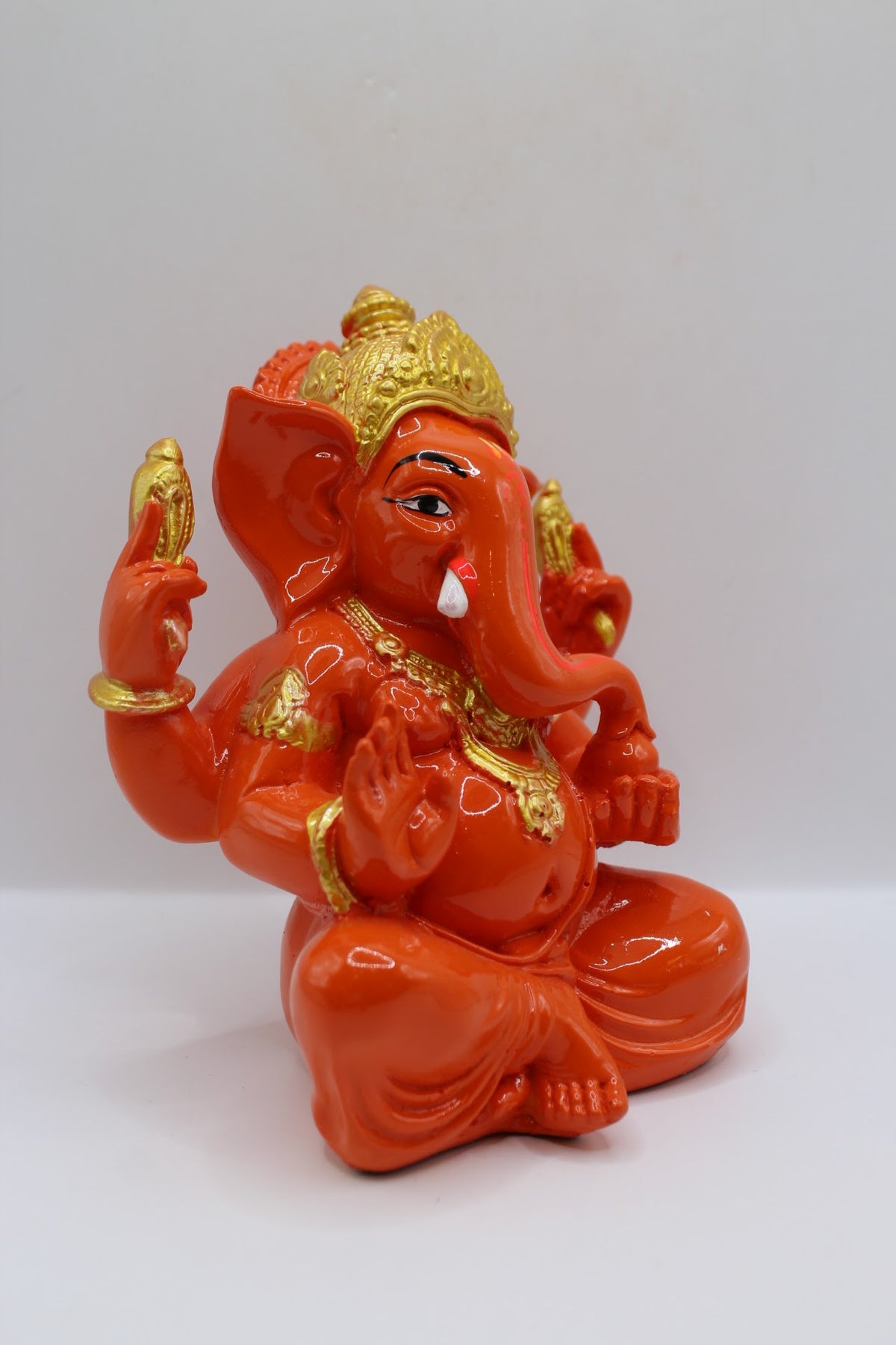 Orange resin Ganesh murti seated, gold crown, left side view