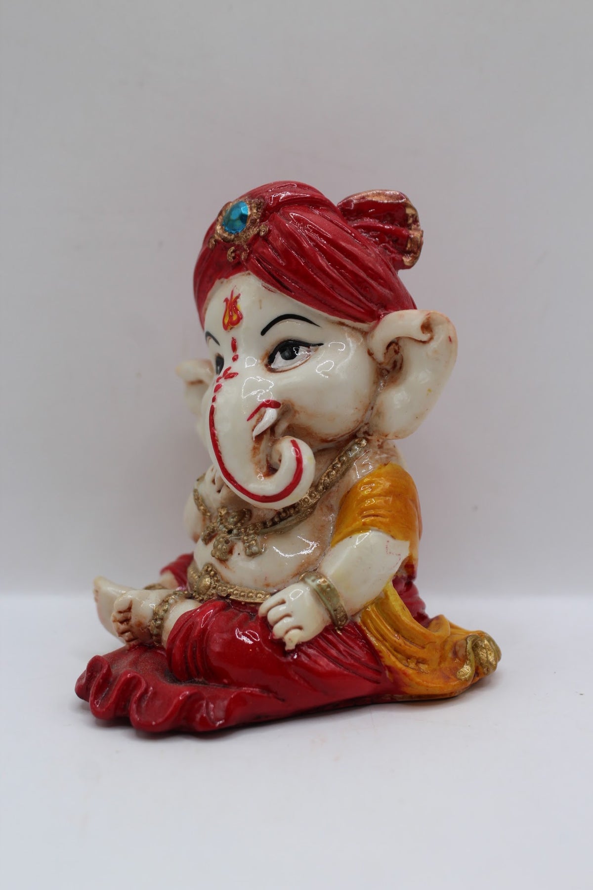 Baby Ganesh murti in red turban, finger to lips, right side view