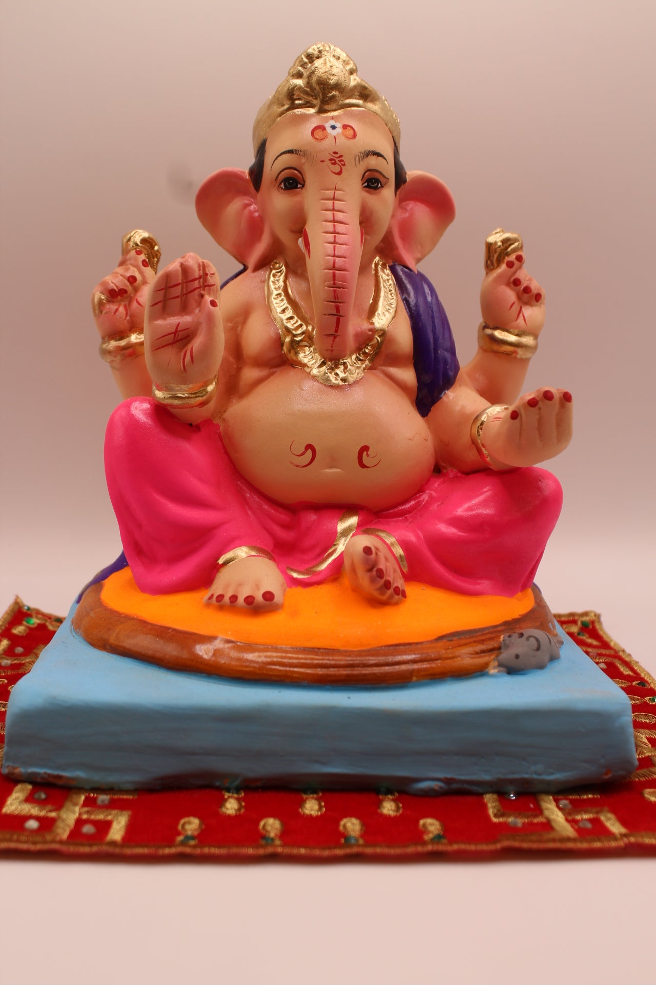 Eco-friendly 8 inch Ganesh Visarjan idol in purple shawl and rani pink dhoti on round cushion – front view