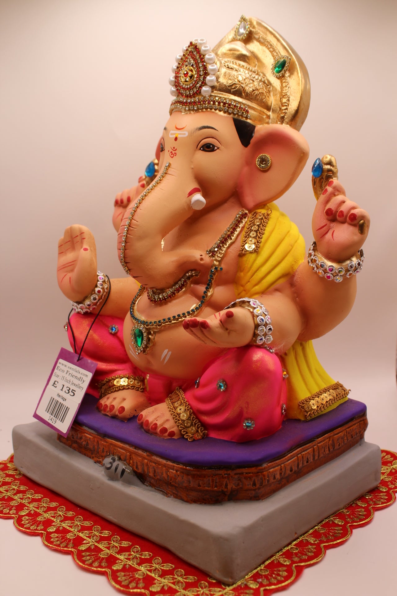 Angled view – jewellery style idol with gold leaf mukut and yellow khes