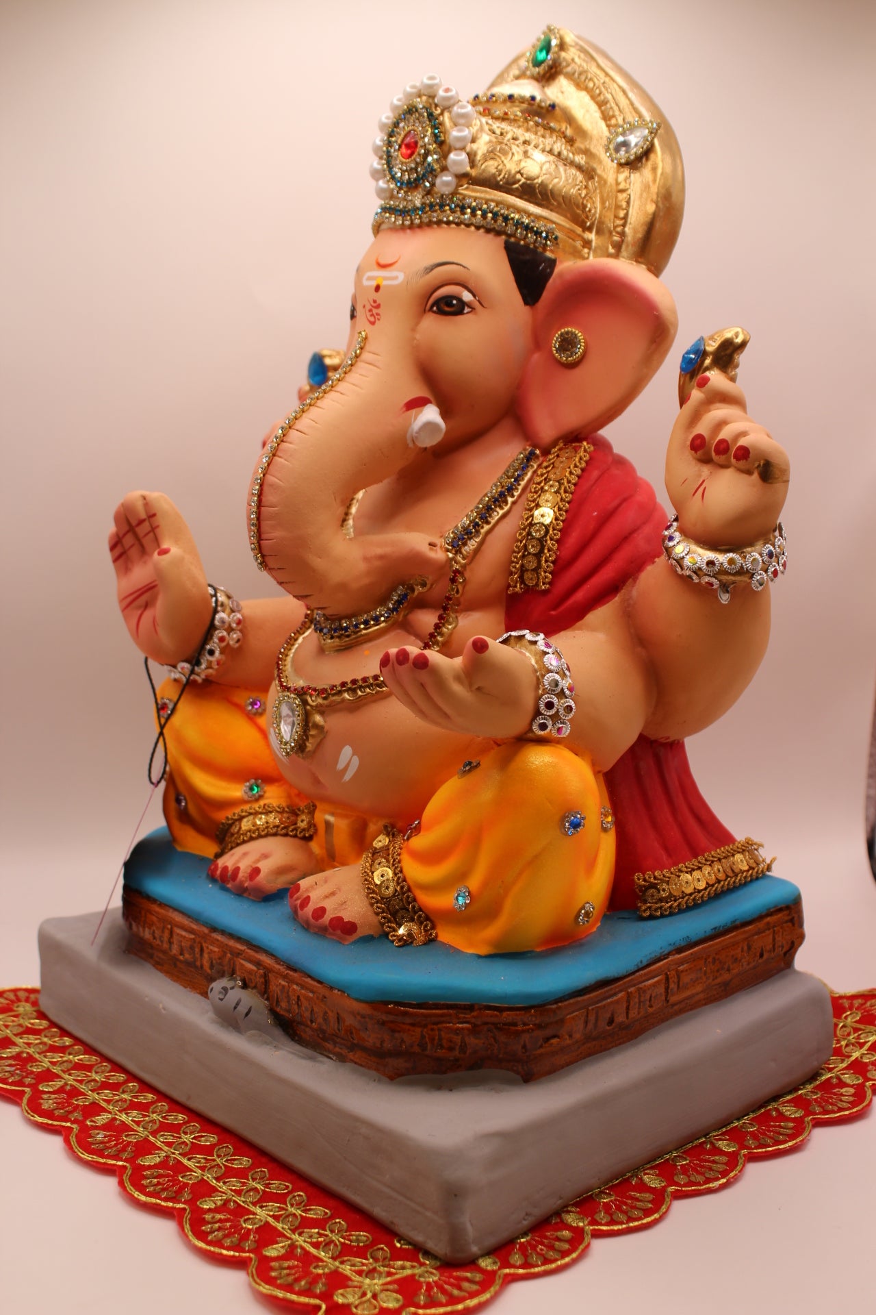 Angled view – jewellery style idol with red khes and orange dhoti