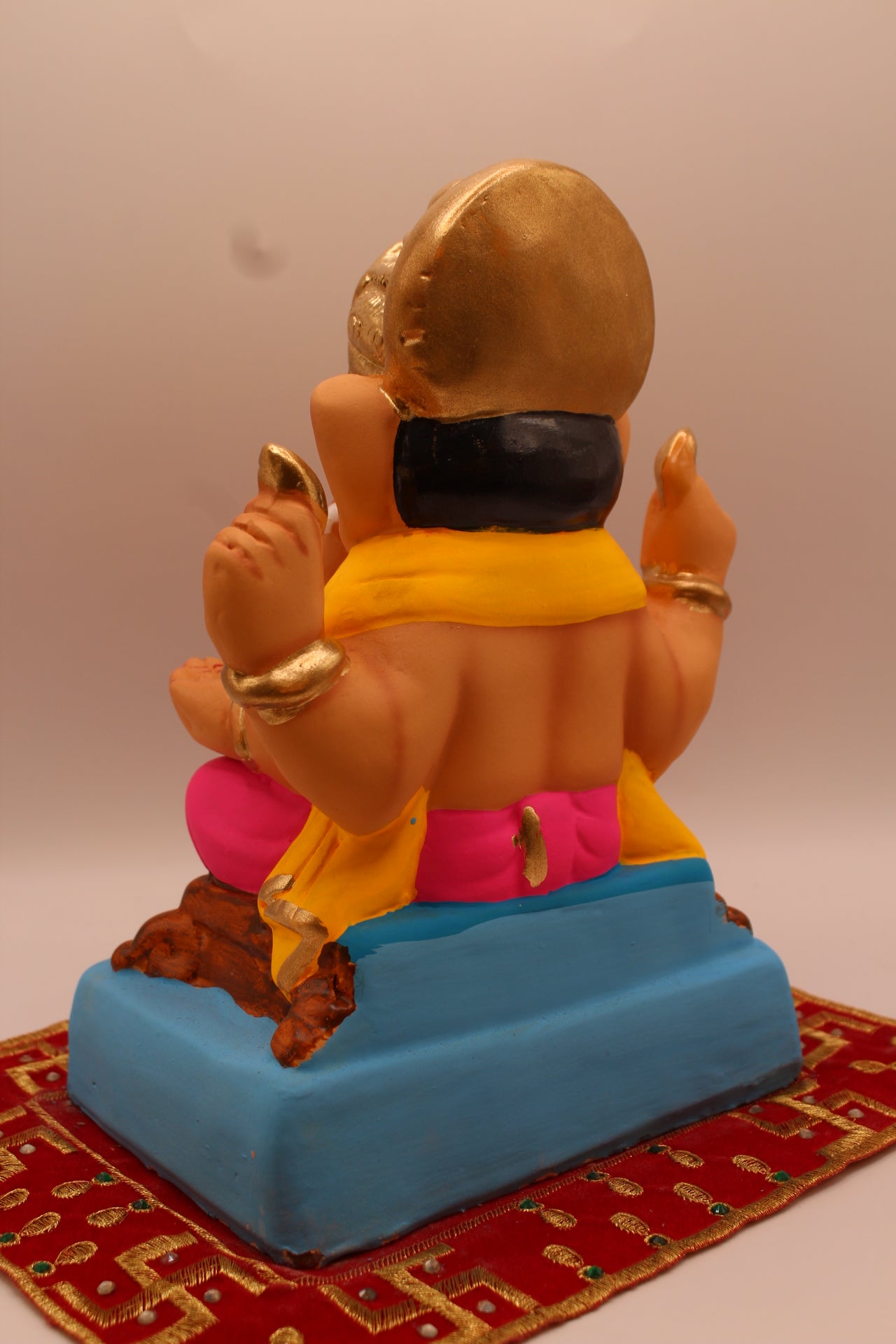 Back view – yellow khes and pink dhoti seated on a wooden chowki