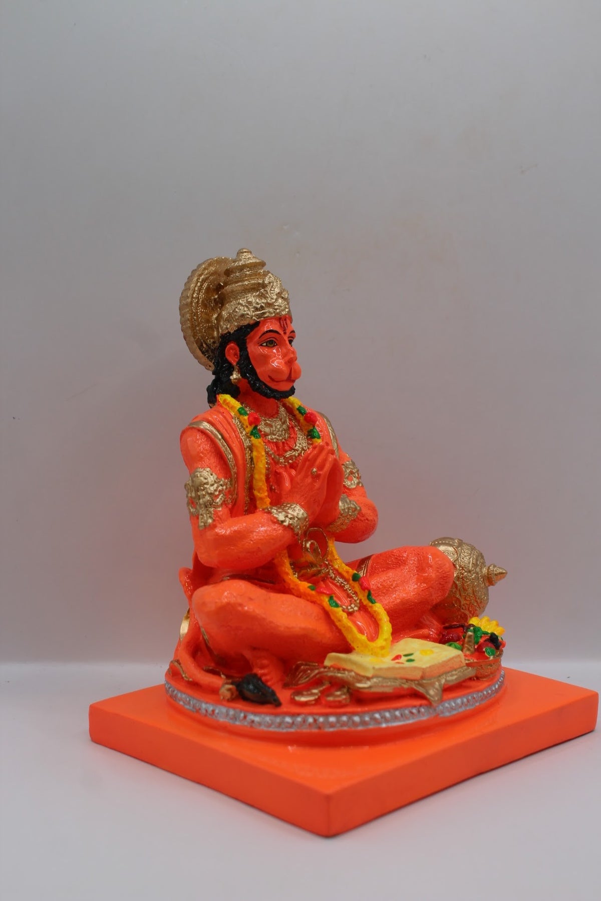 Orange resin Hanuman murti seated in prayer, left side view