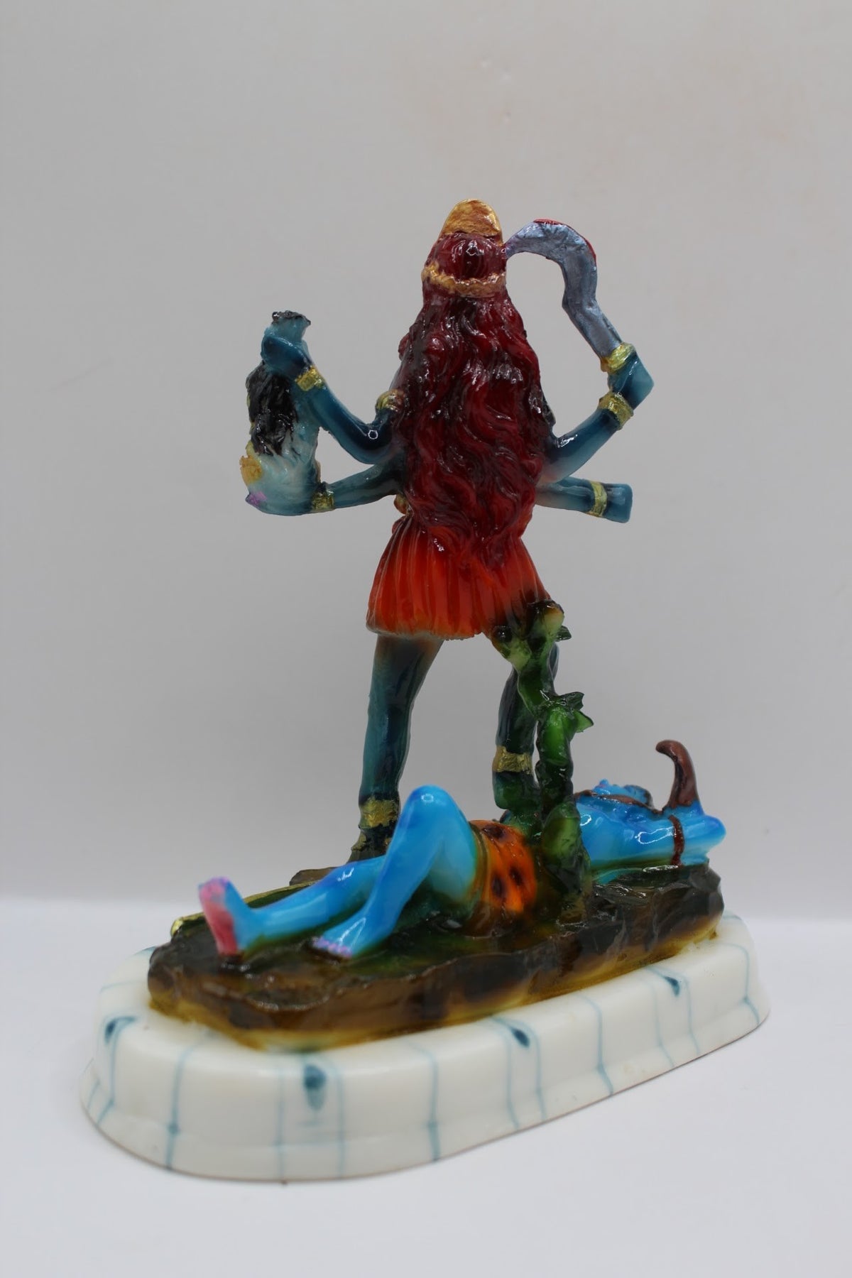 Blue resin Kali Mata murti on a white base, back view