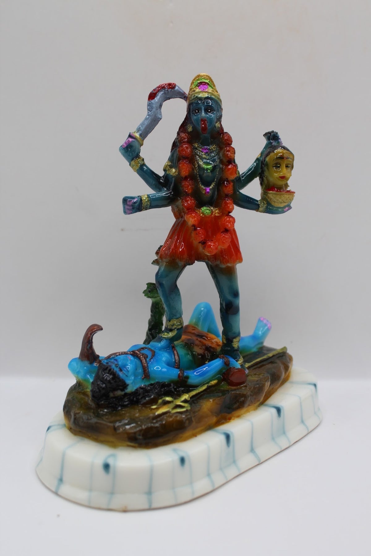 Blue resin Kali Mata murti on a white base, left side view