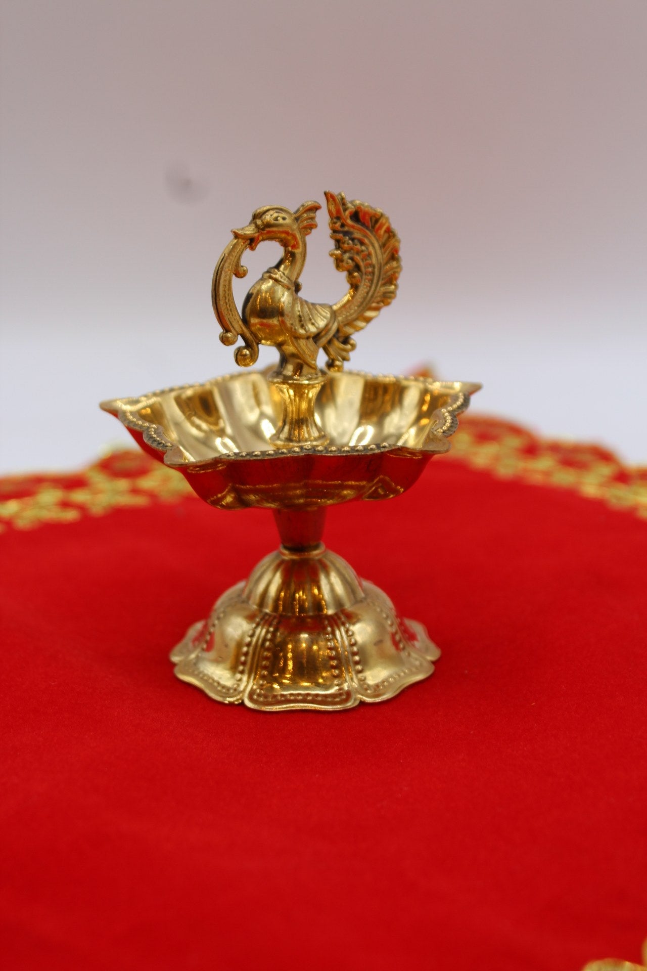 Solid brass peacock diya with a scalloped bowl raised on a fluted pedestal