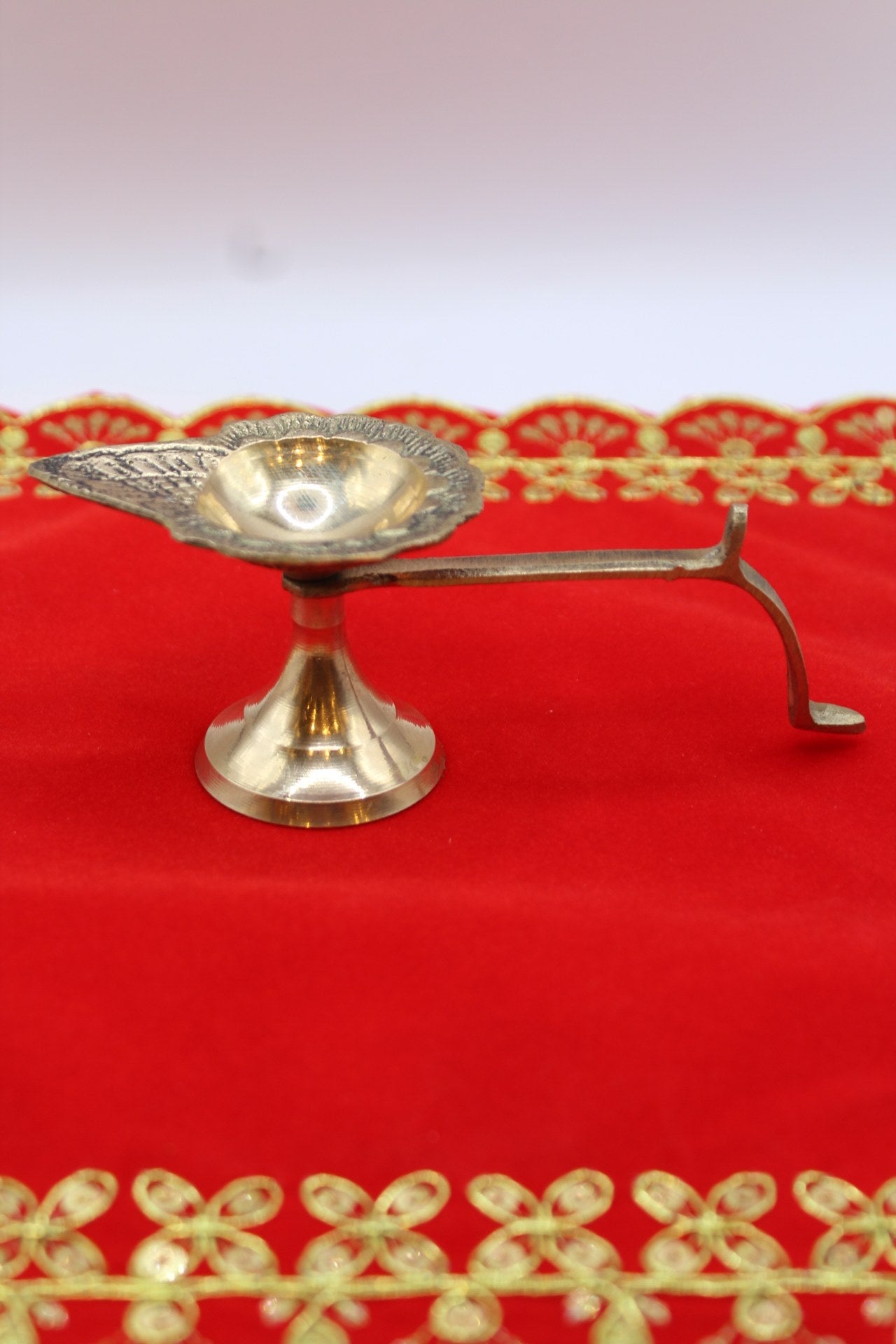 Small footed brass aarti diya with a long side handle and pierced back plate