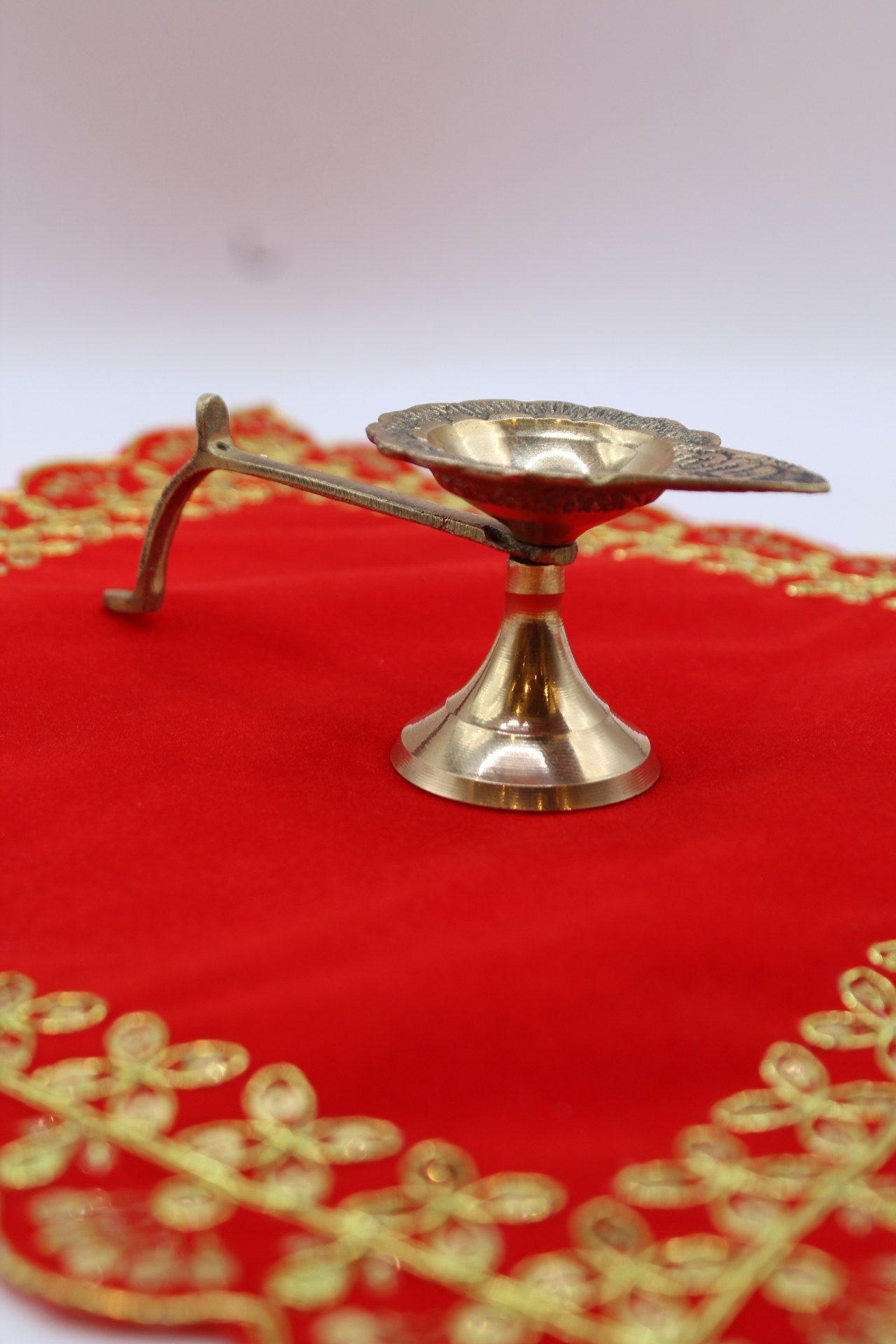 Small footed brass aarti diya with a long side handle and pierced back plate