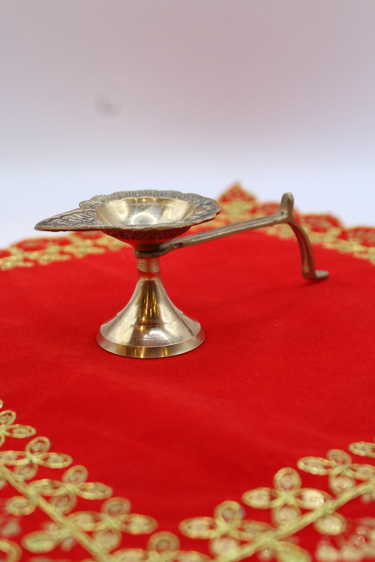 Small footed brass aarti diya with a long side handle and pierced back plate