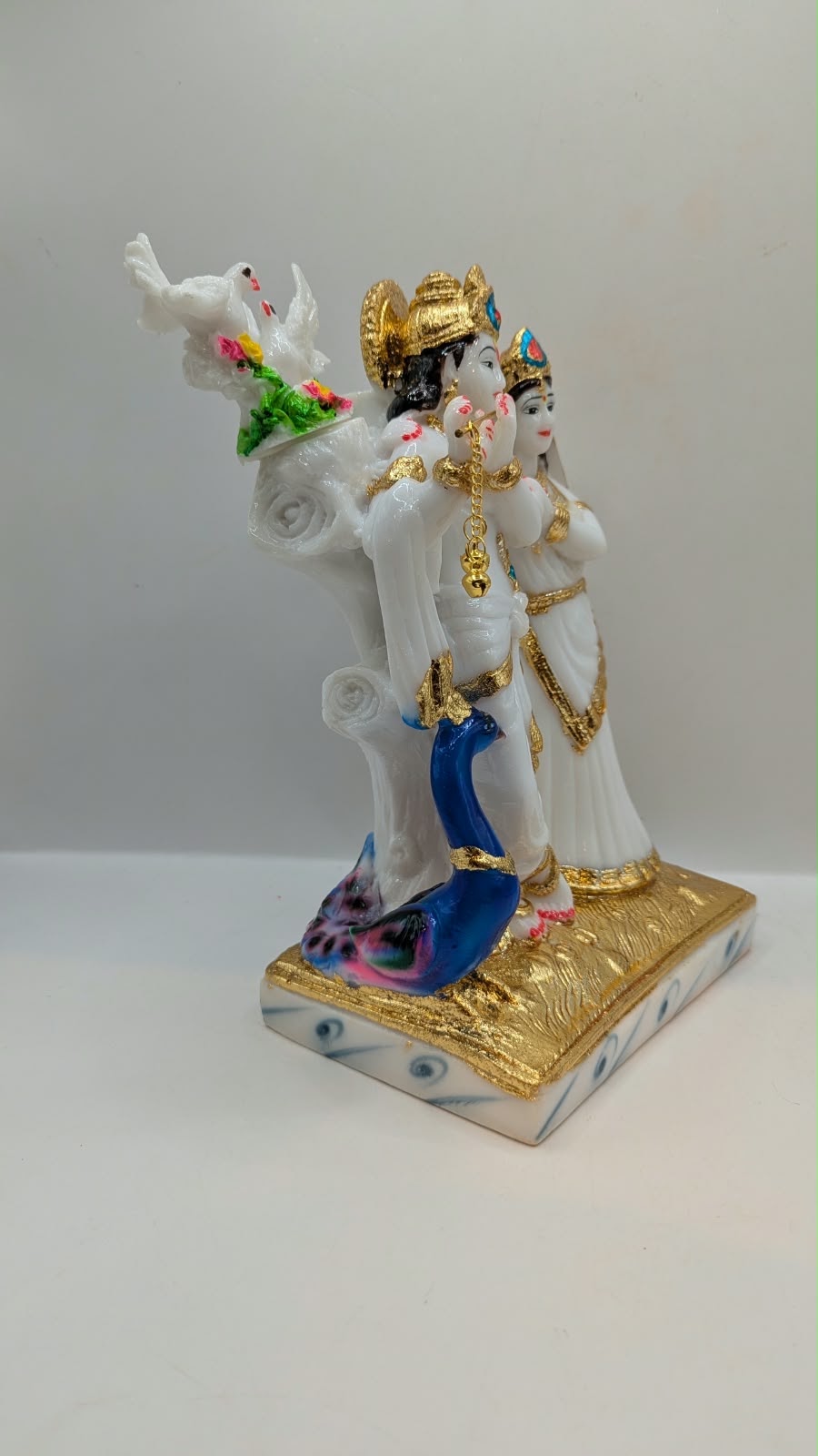 White and gold Radha Krishna statue with peacock, side view