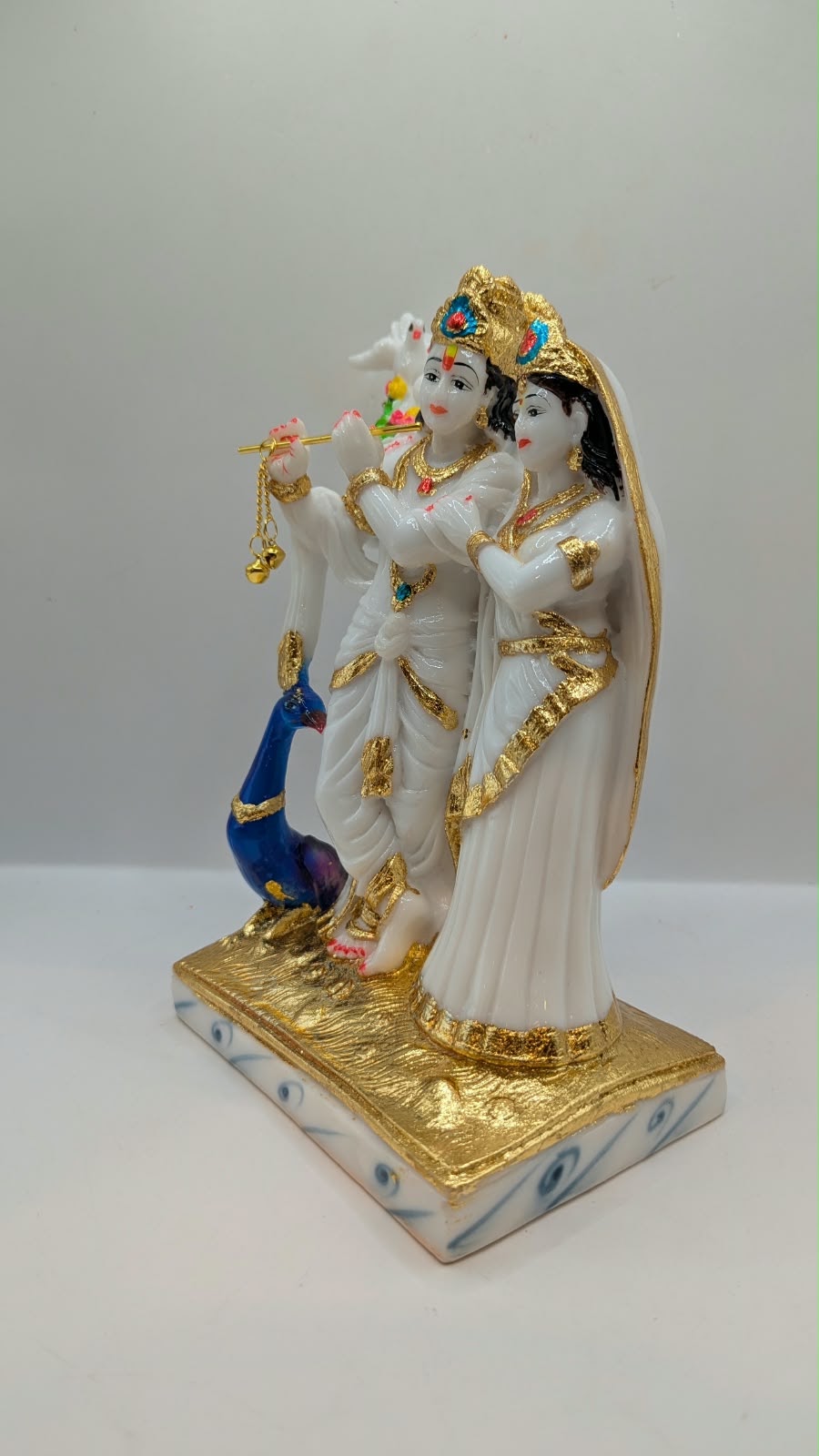 White and gold Radha Krishna statue with peacock, other side view