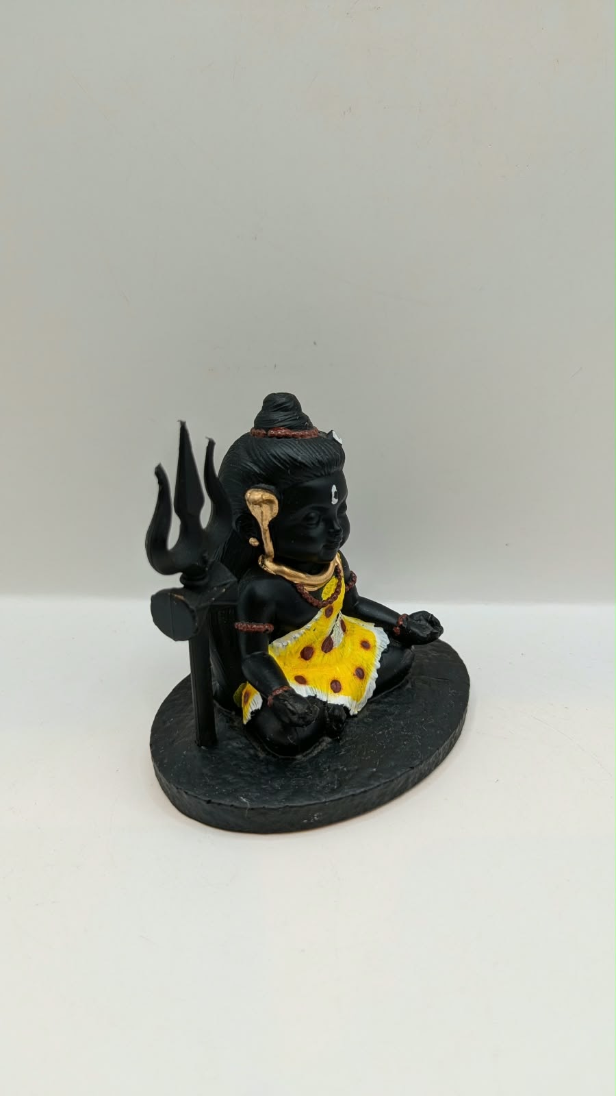 Small black sitting Shiva statue with trishul, side view