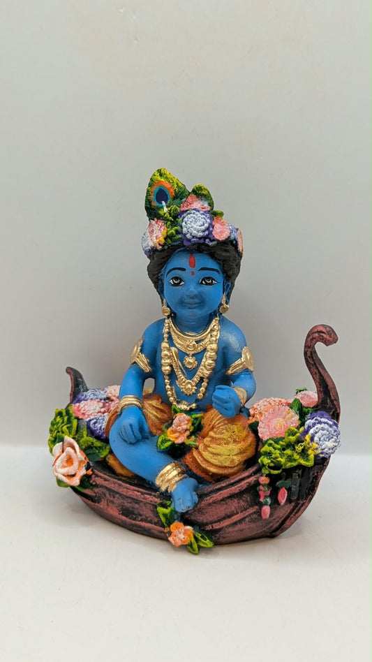 Blue baby Krishna statue on flower boat, front view