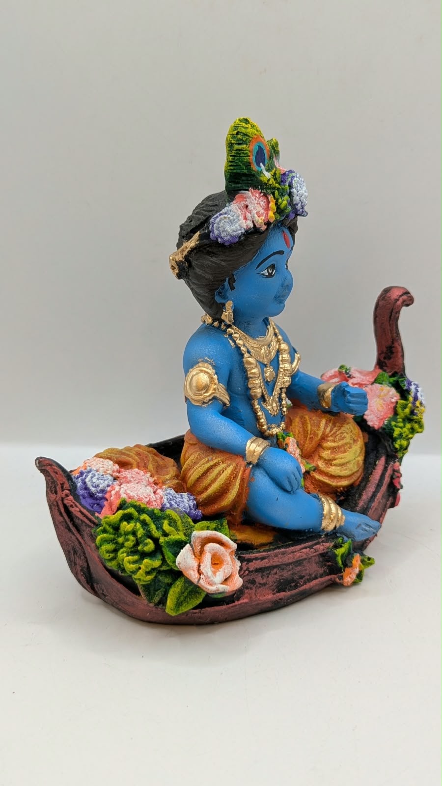 Blue baby Krishna statue on flower boat, side view