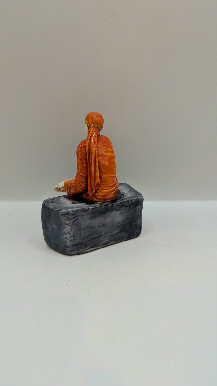 Small Sai Baba statue on grey rock, back view