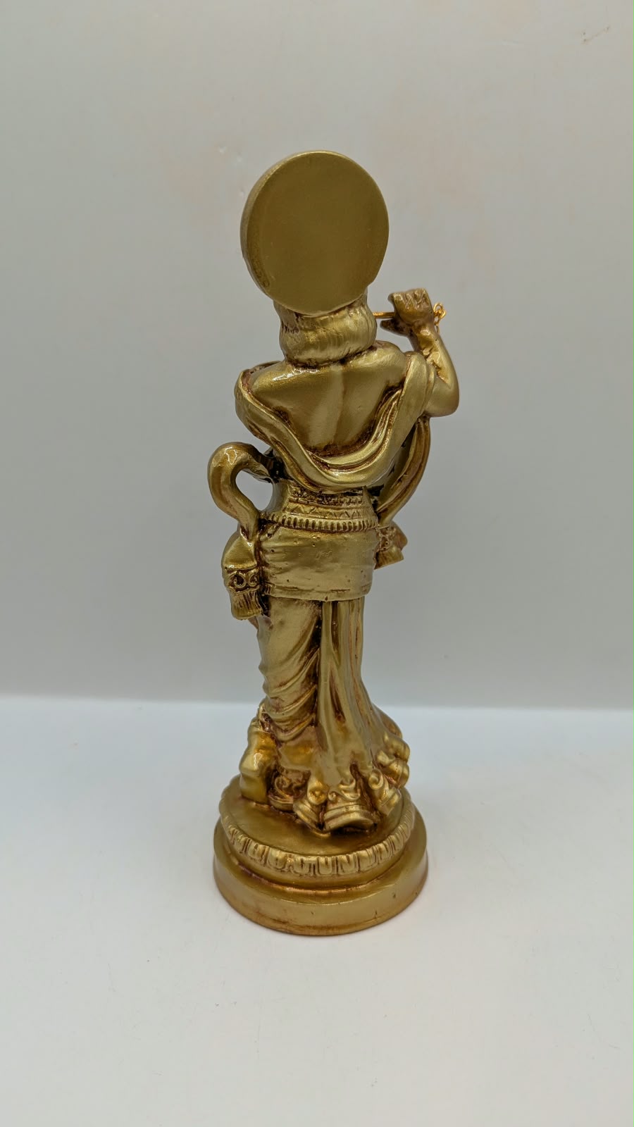 Gold Krishna statue with flute and halo, back view