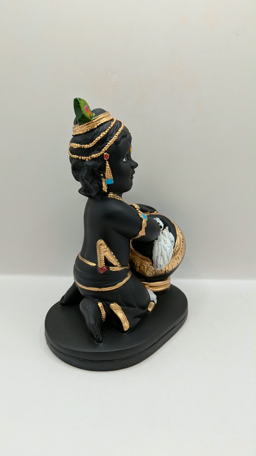 Black and gold baby Krishna statue with butter pot, side view