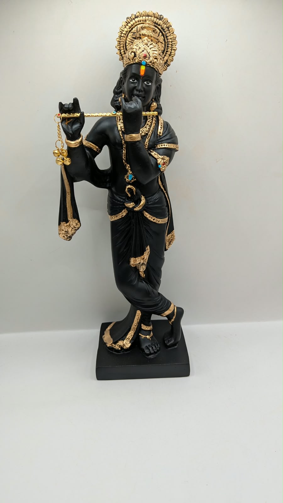 Tall black and gold Krishna statue on square base, front view
