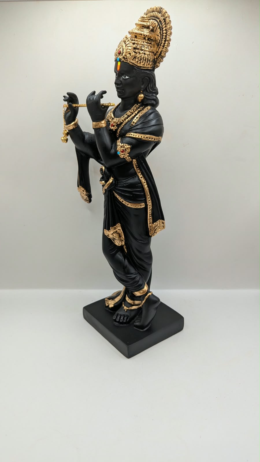Tall black and gold Krishna statue on square base, other side view