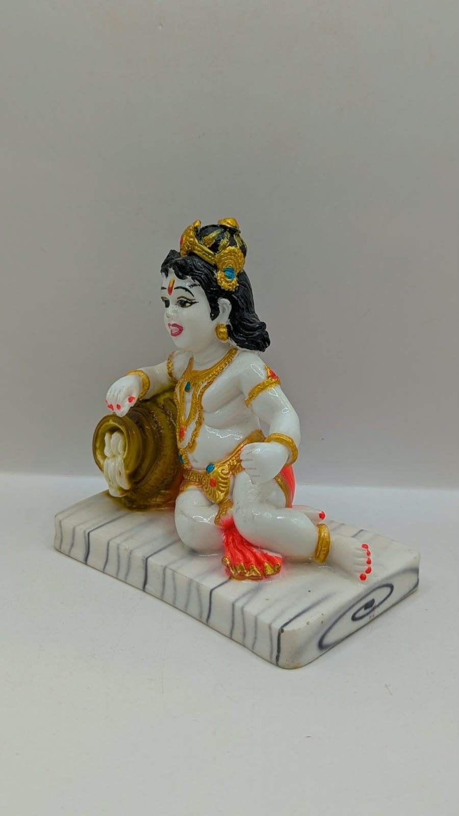 White baby Krishna statue with gold pot and red dhoti, other side view