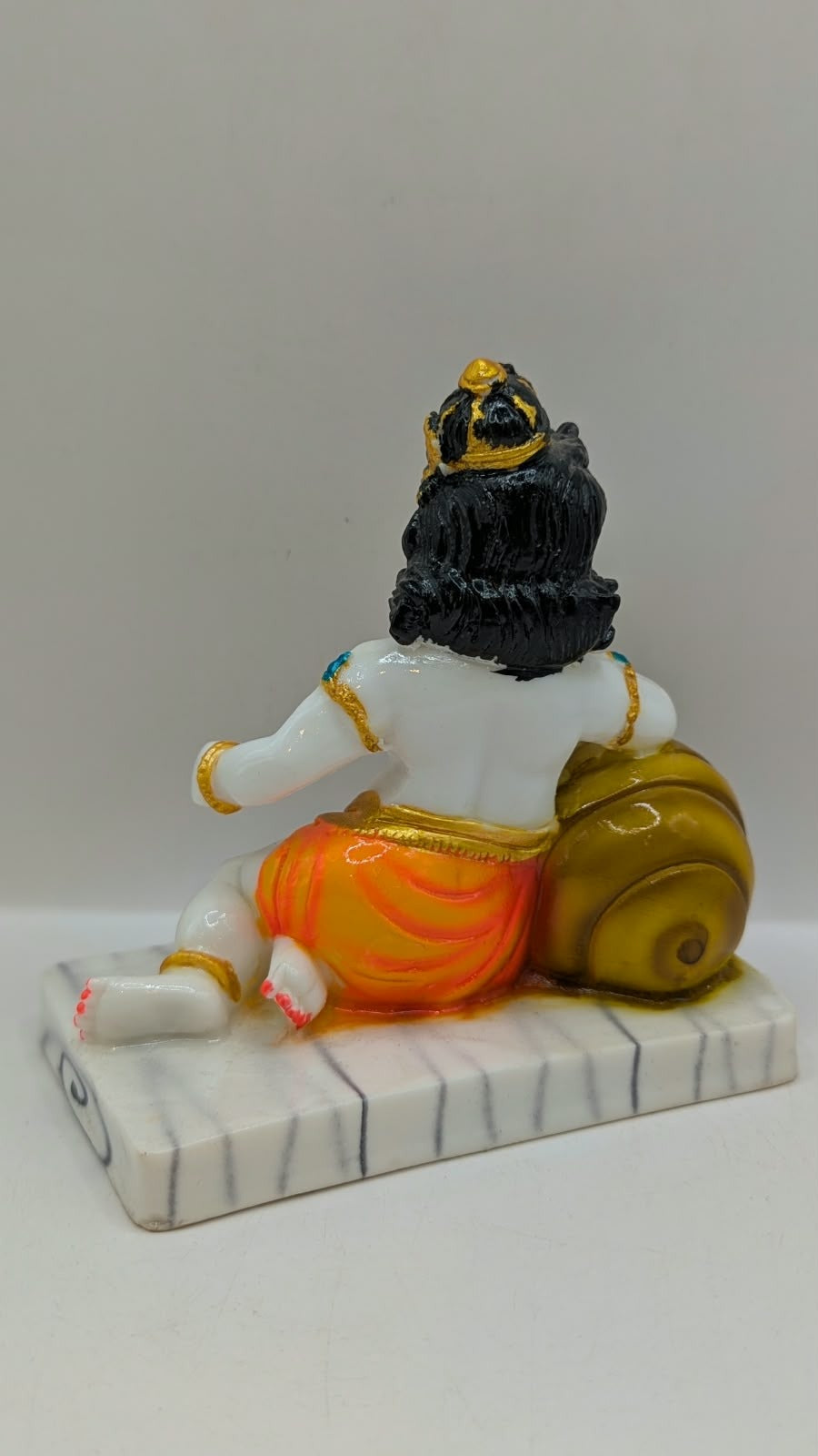 White baby Krishna statue with gold pot and orange dhoti, back view