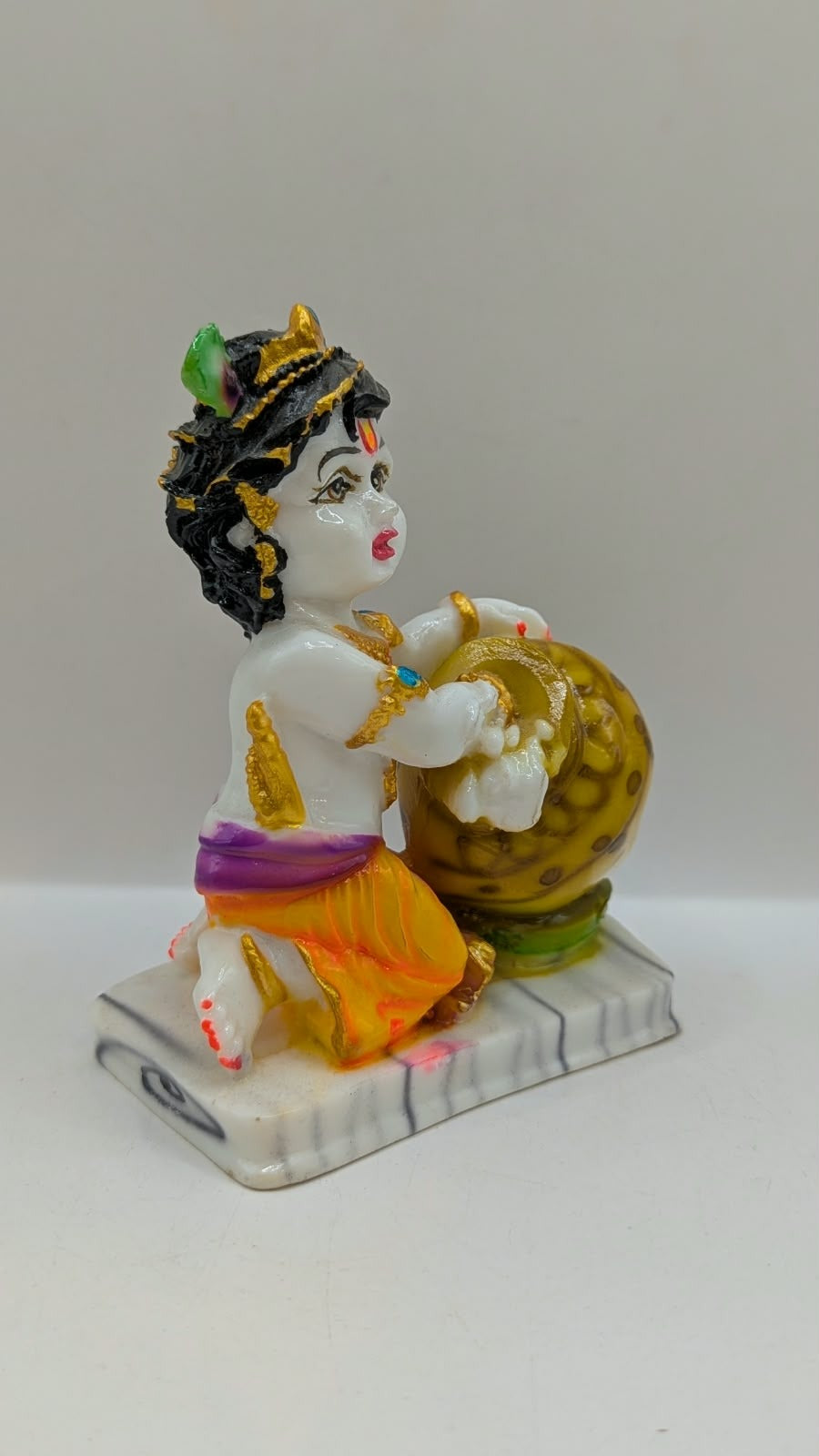 White baby Krishna statue hugging gold butter pot, side view