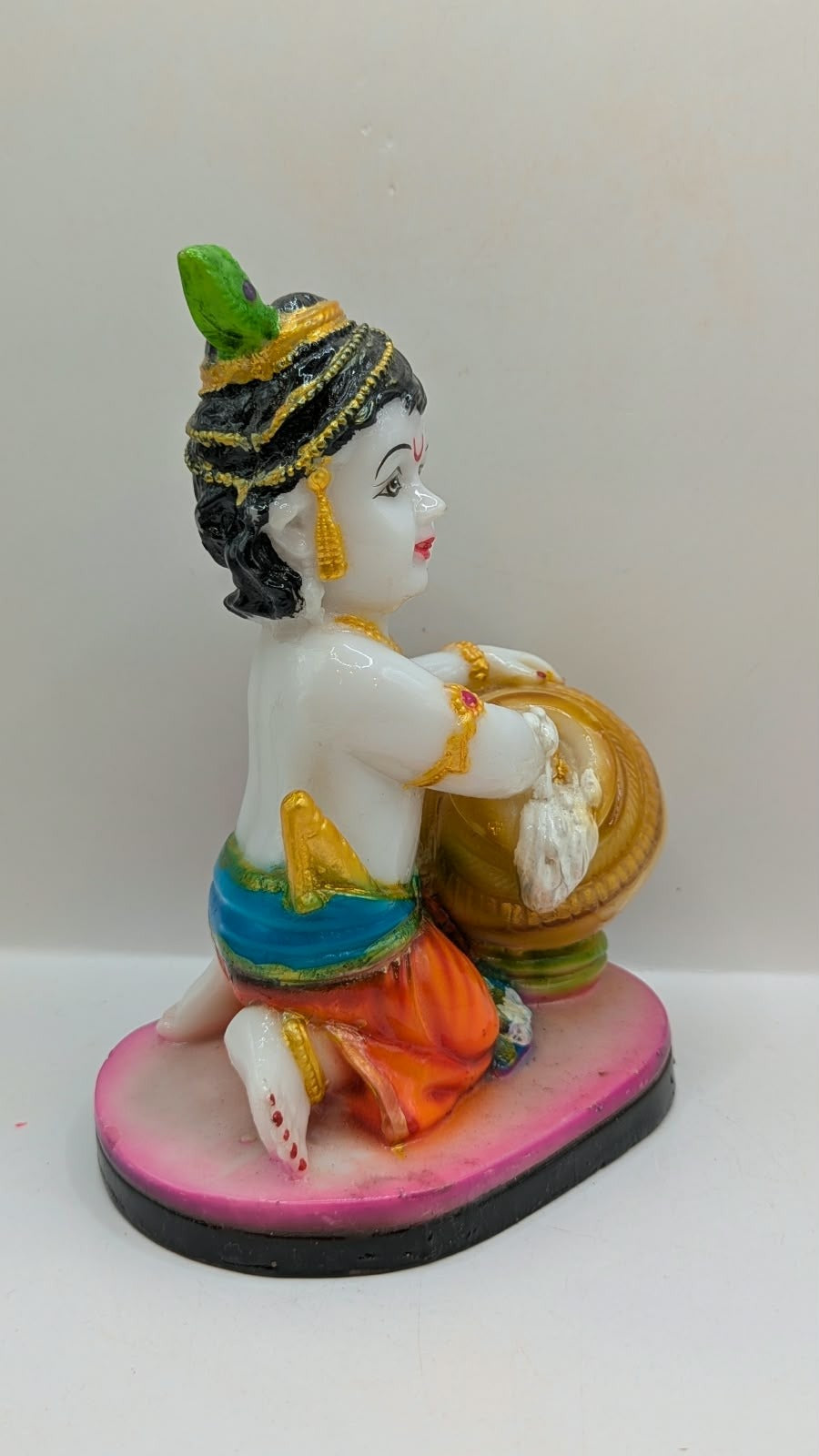 White baby Krishna statue kneeling with butter pot, side view