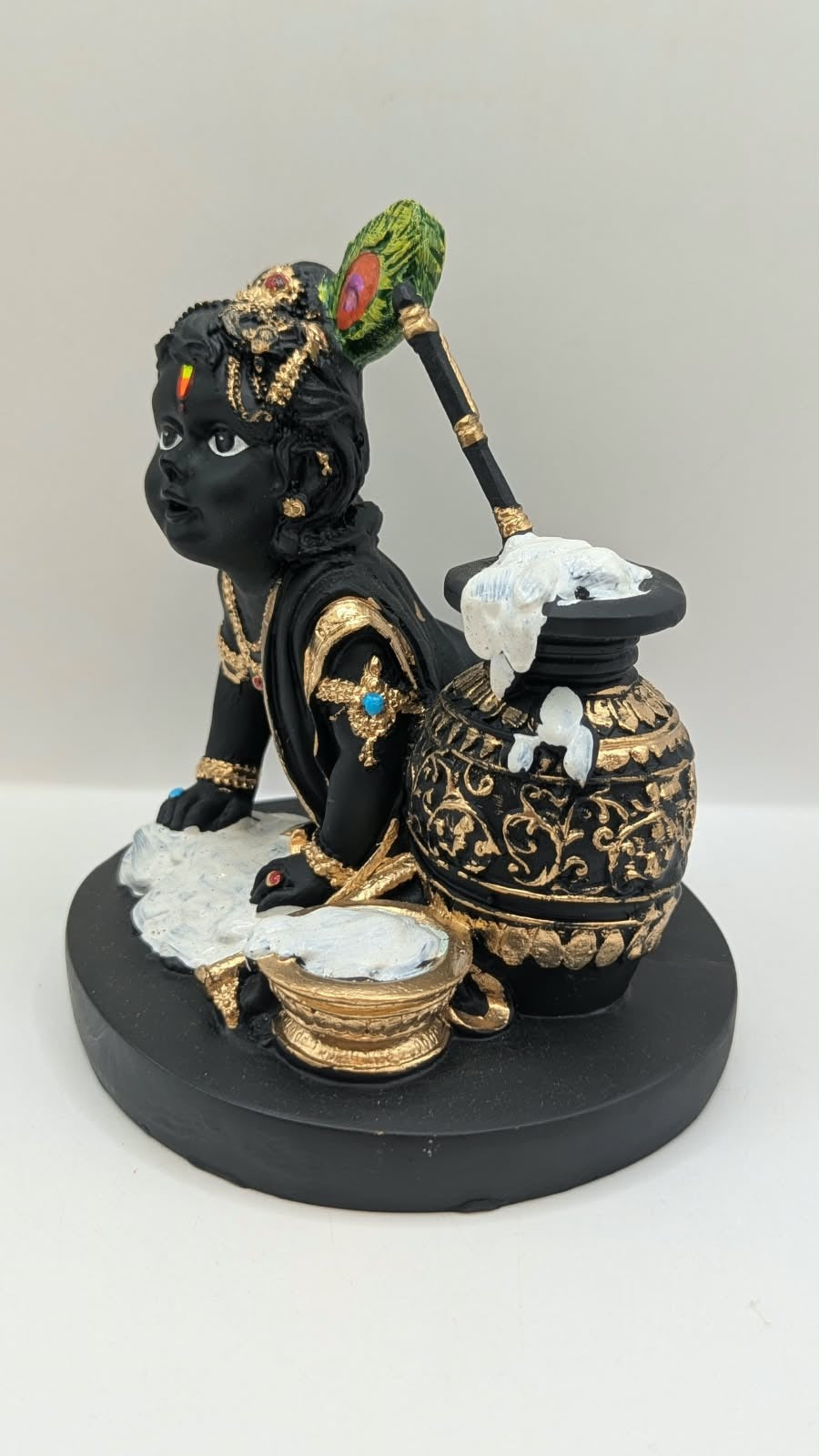 Black and gold baby Krishna statue with butter pot, side view